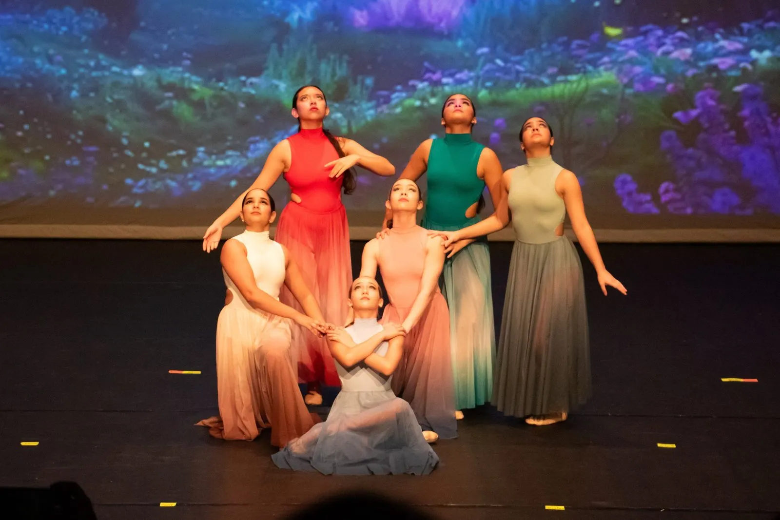 Contemporary group in pastel gowns before a projected forest